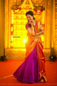 a woman in an orange and purple sari is standing on the floor with her hands clasped to her face