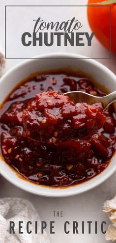 a bowl of tomato chutney with a spoon in it next to some tomatoes