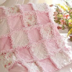 a pink and white blanket sitting on top of a bed next to a vase with flowers