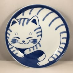 a blue and white plate with a cat on it's side, sitting in front of a wall