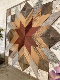 a wooden wall hanging on the side of a building with flowers in front of it