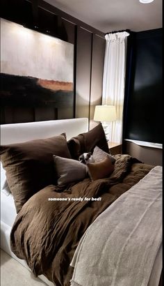 the bed is made with brown linens and pillows, along with a painting on the wall