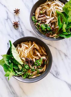 two bowls filled with noodles and vegetables on top of a white marble counter next to anise