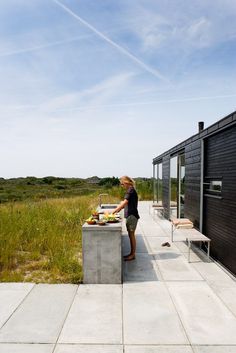 a person standing at a table with food in front of a black building and grassy field