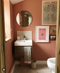 a bathroom with pink walls and pictures on the wall above the toilet, sink and mirror