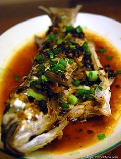 a white plate topped with fish covered in sauce and garnished with green onions