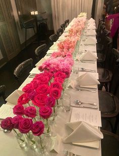 a long table with many vases filled with pink and red flowers on each side