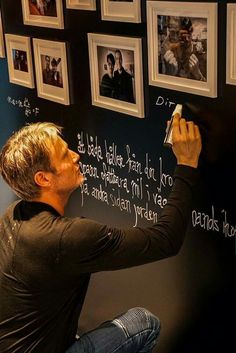 a man writing on a blackboard with pictures hanging on the wall behind him,