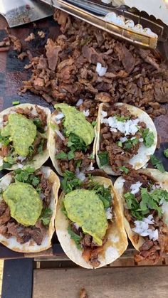 several tacos with meat and guacamole on them sitting on a table