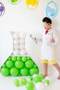 a young boy standing in front of a green and white science experiment with lots of balloons