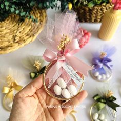 a hand holding a small jar filled with candies on top of a white table