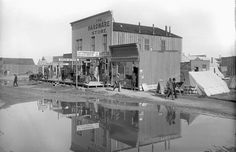 an old black and white photo of people standing in front of a building next to a body of water