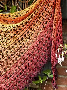 a crocheted shawl hanging on a brick wall next to flowers and plants