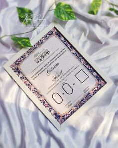 the wedding card is laying on top of white sheets and green leafy leaves are scattered around it