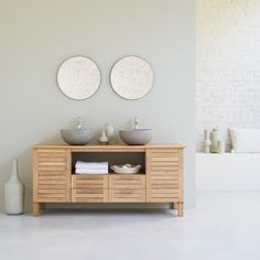 two circular mirrors on the wall above a wooden cabinet with drawers and sinks in front of it