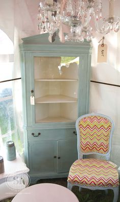 a chair sitting in front of a china cabinet with a chandelier above it