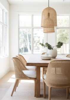 a dining room table with chairs and a potted plant in the center, next to large windows