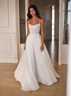 a woman in a white wedding dress standing on the floor with her hand on her hip