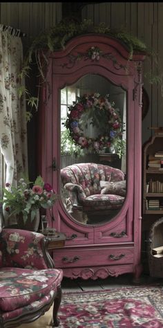 a pink armoire sitting in front of a mirror and chair next to a window