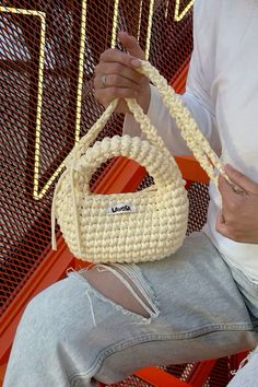 a woman sitting on a chair holding a white handbag in front of her face