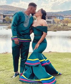 a man and woman standing next to each other in front of a lake