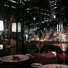 two plates with food and wine on a table in front of a cityscape