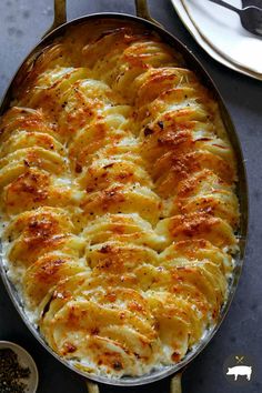 a casserole dish with potatoes and cheese in it on a table next to silverware