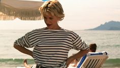 a woman is standing on the beach with her back to the camera, wearing a black and white striped shirt