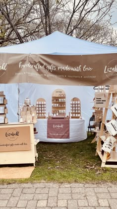 an outdoor market with wooden crates and signs on the grass, under a large tent