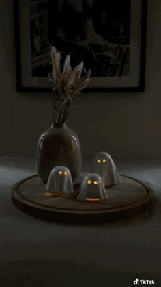 three white ghost heads sitting on top of a wooden plate in front of a painting