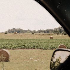 some hay bales sitting in the middle of a field next to a car window