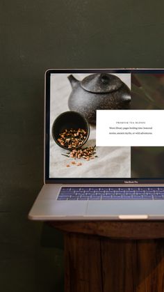 an open laptop computer sitting on top of a wooden table next to a teapot