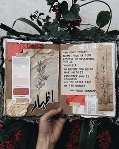 an open book with writing on it in front of a plant and other items that include flowers