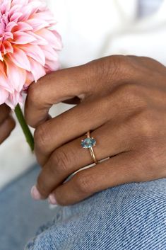 a woman's hand holding a pink flower with a gold ring on her finger