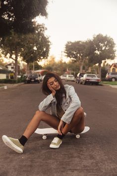 a woman is sitting on a skateboard in the middle of the street and touching her shoe