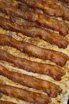 bacon strips are lined up on a baking sheet ready to be cooked in the oven