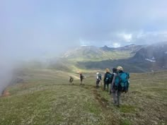 three people hiking up a hill in the mountains on a foggy day with backpacks