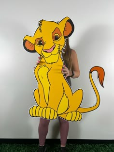 a woman holding up a cardboard cutout of a cartoon character from the lion king