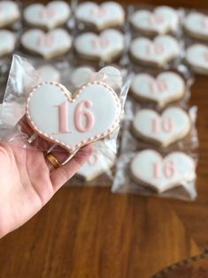 a hand holding a heart shaped cookie with the number sixteen on it in front of other cookies