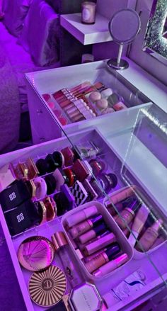 an assortment of makeup products displayed in a purple lit display case on a table next to a mirror