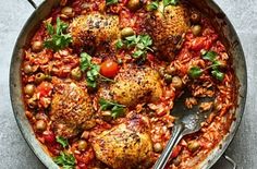 a skillet filled with chicken and tomatoes covered in sauce, garnished with parsley