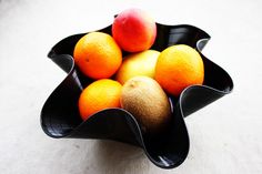 a black bowl filled with oranges and apples