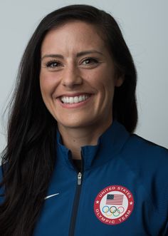 a smiling woman in a blue jacket with an american flag on her chest and the olympic badge