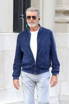 an older man with grey hair wearing sunglasses and a blue jacket is walking down the street