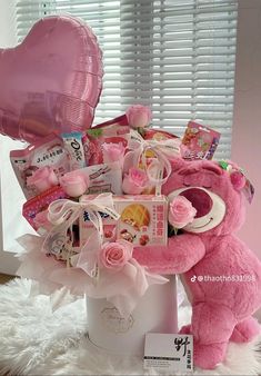 a pink teddy bear sitting next to a heart shaped balloon in a white vase filled with baby items