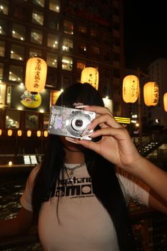 a woman holding up a camera in front of her face with chinese lanterns behind her