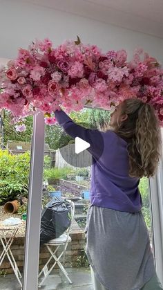 a woman is standing in front of a window with pink flowers on her head and arms