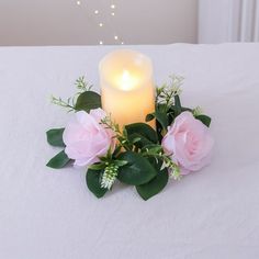 a lit candle and some pink flowers on a white table cloth with lights in the background