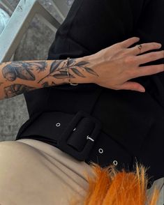 a woman with tattoos on her arm and hand next to a stair case holding an orange hair