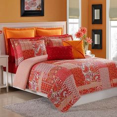 an orange and red bed in a bedroom next to a white table with flowers on it